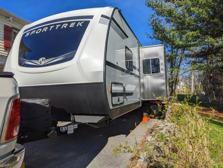 A white SPORTTREK travel trailer with an extended side slide-out is parked on a driveway, ideal for an rv rental or camping.. Sport Trek Sport Trek Trailer 2021