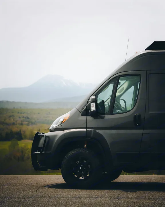 Adventure-ready dark grey RV rental van, with off-road tires and bull bar, parked on a road overlooking mountains.. Dodge Ram Promaster 3500 2021