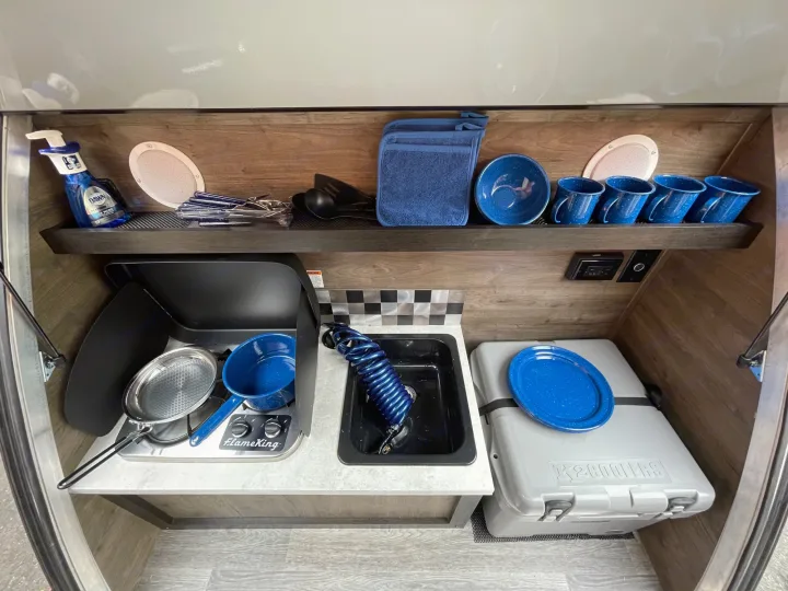 This RV rental's compact kitchen offers essential camping amenities, including a stove, sink, cooler, and dishes for convenient travel.. Braxton Creek Bushwhacker 2022