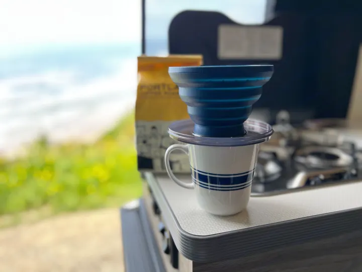 Coffee brewing in an RV rental: blue pour-over, striped mug on a counter with ocean views and coffee bag.. Winnebago Solis 2023