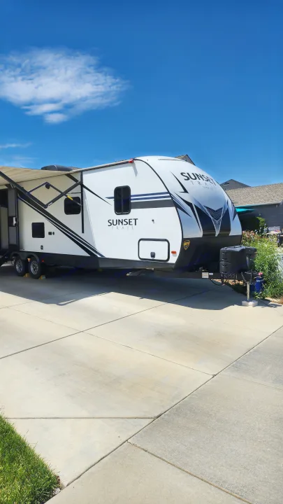 A white and black Sunset Trail travel trailer is parked on a concrete driveway, ready for an RV rental trip.. Crossroads RV Sunset Trail Super Lite 2019