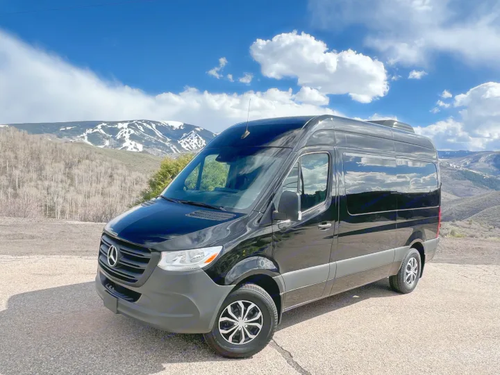 Black Mercedes Sprinter van, perfect for RV rental adventures, parked against a scenic snowy mountain landscape.. Mercedes-Benz Sprinter 2023