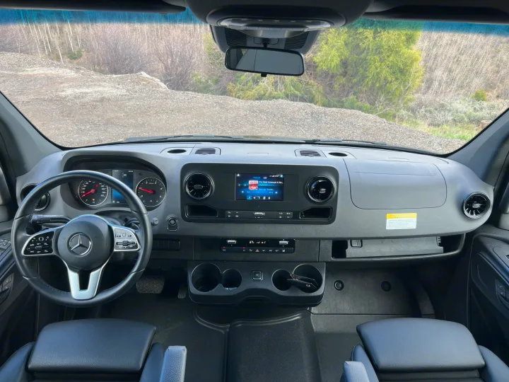 Inside an RV rental: driver's perspective of a sleek Mercedes-Benz dashboard, steering wheel, and infotainment screen.. Mercedes-Benz Sprinter 2023