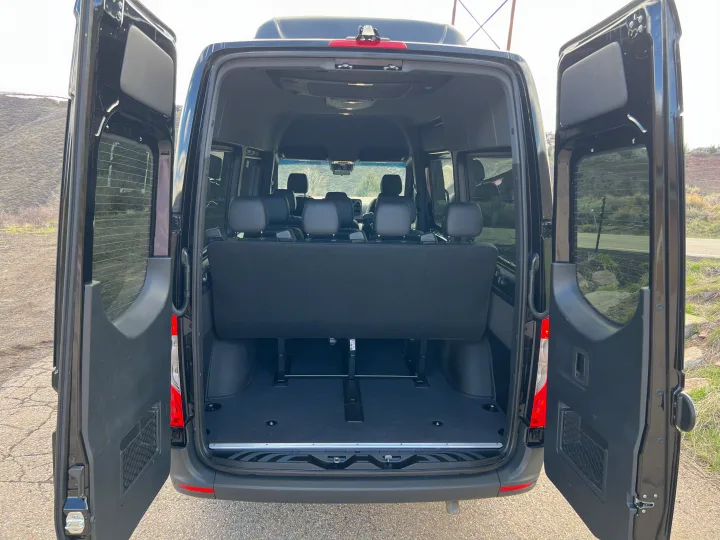 Rear view of a black passenger van's open doors revealing its interior with seats and ample cargo space, ideal for rv rental.. Mercedes-Benz Sprinter 2023