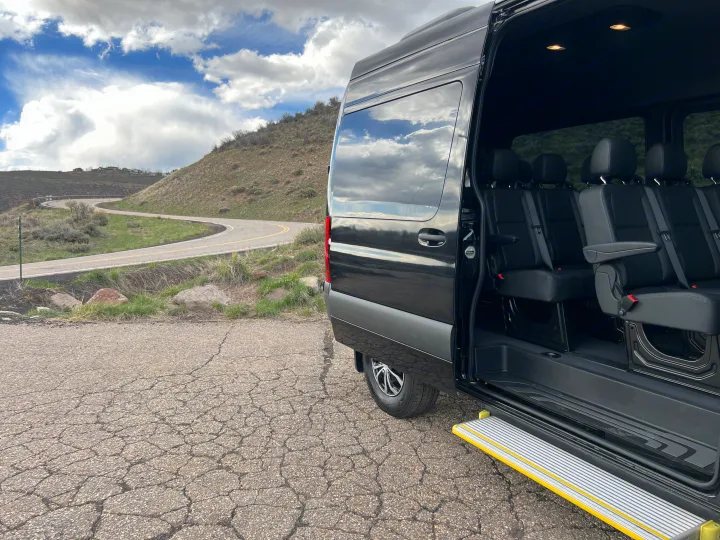 Black luxury passenger van for RV rental, door open to seats and step. Parked on a cracked road by hills and winding path.. Mercedes-Benz Sprinter 2023