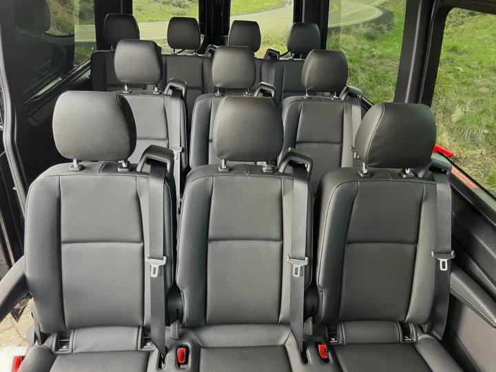 Inside a luxurious RV rental: multiple rows of black passenger seats with safety belts and ISOFIX anchors visible.. Mercedes-Benz Sprinter 2023