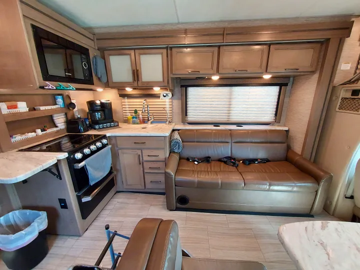 Inside an RV rental, featuring a full kitchen with stove, microwave, sink, and a comfortable brown leather couch.. Thor Coleman 2021