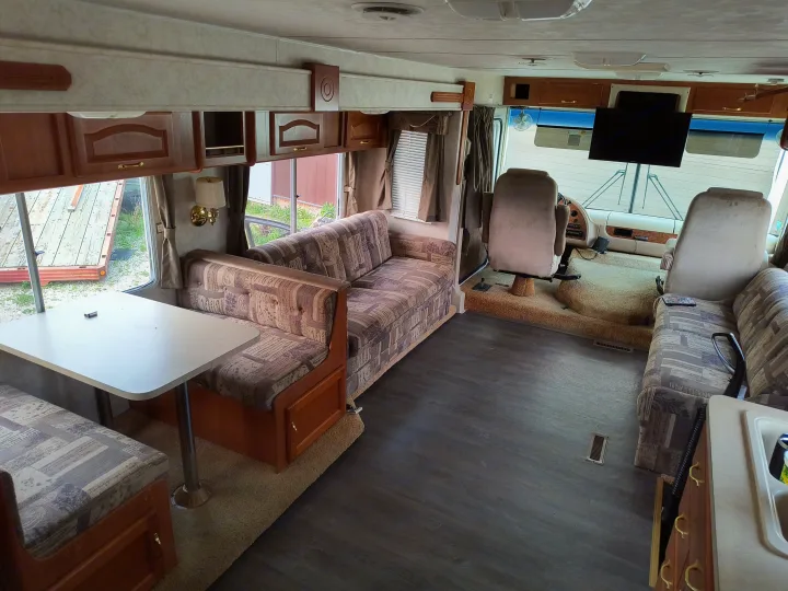 Spacious rv rental interior features a patterned sofa, dinette, and cockpit. Overhead cabinets & modern flooring seen.. Damon Corporation Daybreak 2001
