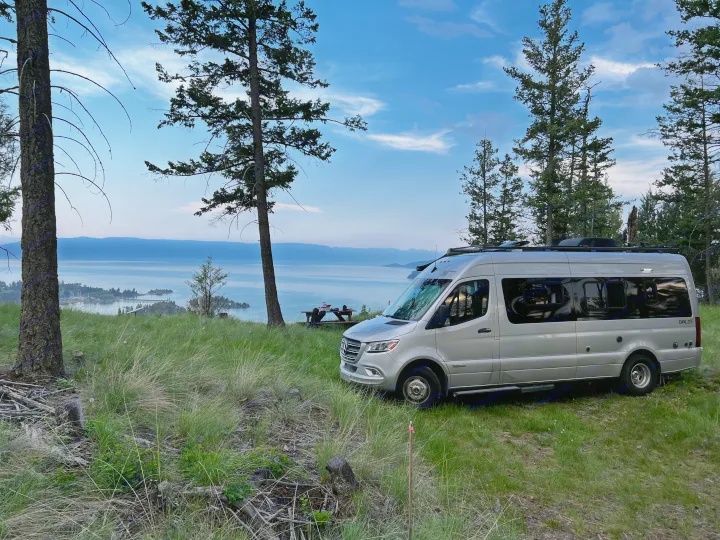 An RV rental, a silver Winnebago Boldt campervan, parked overlooking a scenic lake and mountains at dusk.. Winnebago Boldt 2020