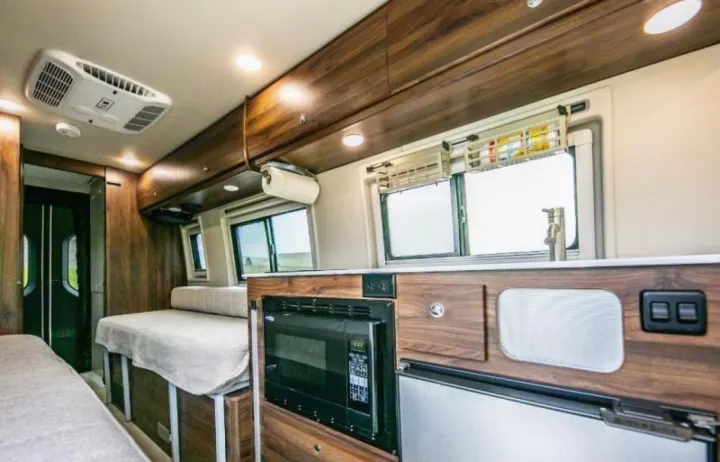 Inside an RV rental: a well-equipped kitchen with microwave, fridge & sink, and comfortable living/bedding for travel.. Winnebago Boldt 2020