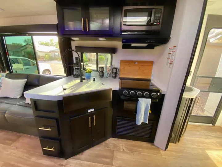 Sleek RV rental interior: a fully equipped kitchen (microwave, stove, sink) and living area with a dark sofa.. Forest River Cherokee Grey Wolf 2022