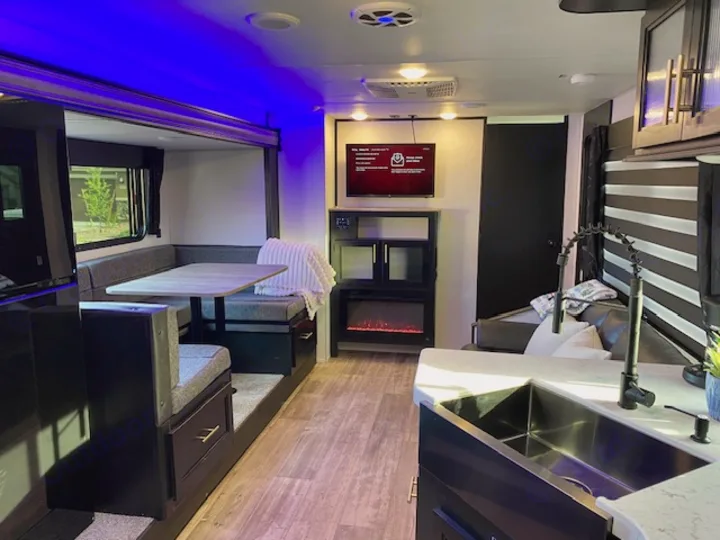 Modern rv rental interior: dinette, kitchen with sink, living area with TV & electric fireplace. Blue accent lighting.. Forest River Cherokee Grey Wolf 2022