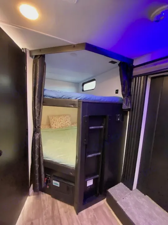 This RV rental features stacked bunk beds with privacy curtains, a ladder, and cozy lighting for a comfortable travel stay.. Forest River Cherokee Grey Wolf 2022