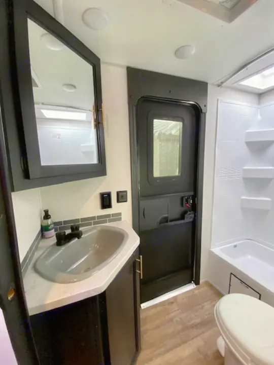 Compact RV rental bathroom: dark vanity with gray sink, black mirror cabinet, shower/tub, toilet, & wood-look floor.. Forest River Cherokee Grey Wolf 2022
