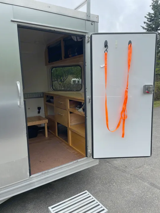 Open door of an RV rental showing custom wood interior, storage, and a view outside. Mobile living.. Weeroll Silver cloud 2020