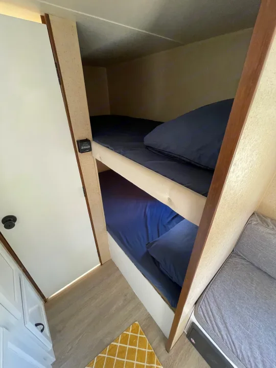 RV rental bunk beds with blue bedding & a compact sleeping area. Features include a door, control panel, and gray seating.. Jayco Jay Flight SLX 2015