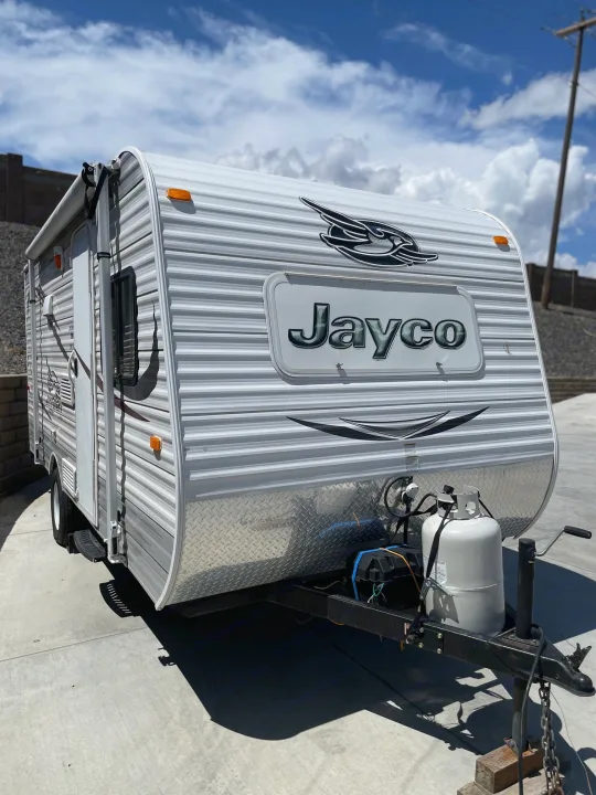 Bright white Jayco travel trailer, ideal for RV rental. Front propane tanks visible, parked outdoors on concrete.. Jayco Jay Flight SLX 2015