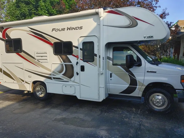 This white Thor Four Winds Class C RV rental, featuring decorative graphics, is parked on an asphalt driveway.. Thor Four Winds 2020