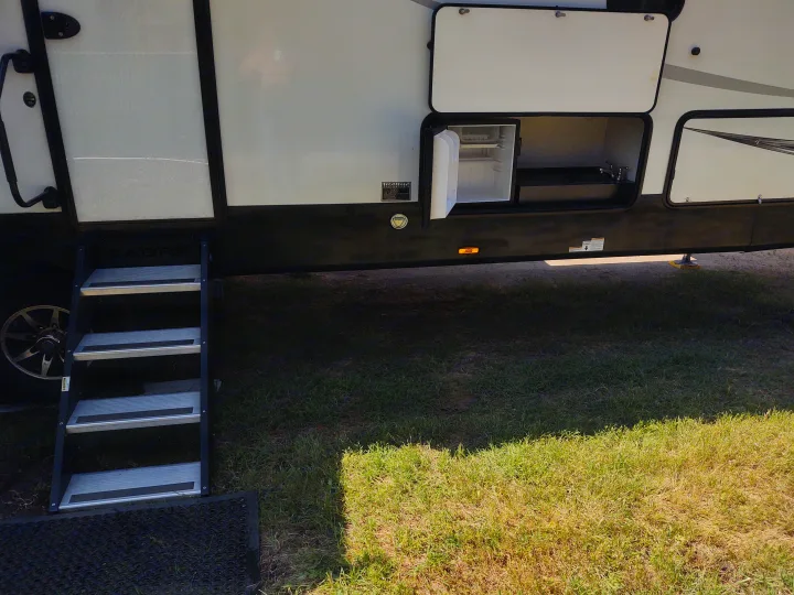 Side of an RV rental: extended steps, outdoor mini-fridge, and sink setup. Perfect for camping adventures!. Forest River Sabre 2021