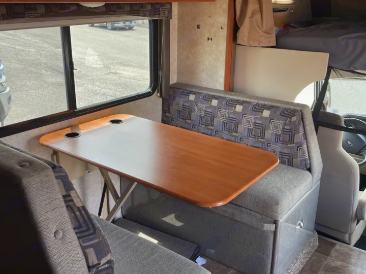 This RV rental interior shows a dinette with a wooden table, cupholders, comfortable benches, and an overhead sleeping area.. Adventurer Adventurer Motorhome 2017