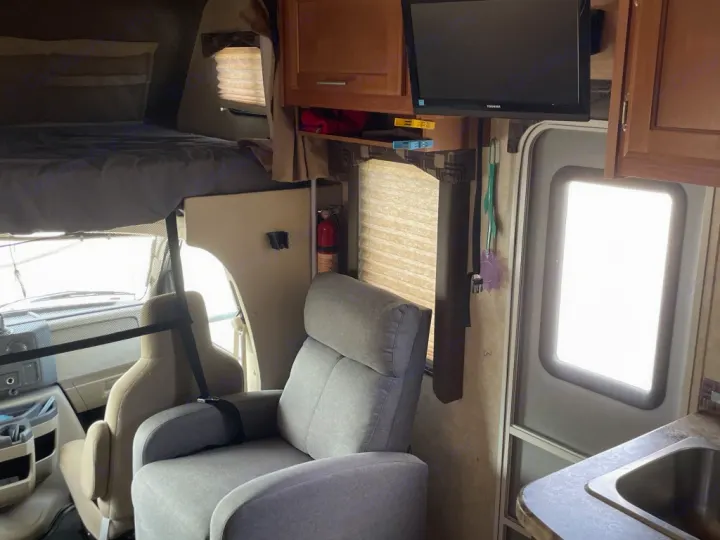 View inside an RV rental. Features include an overhead bunk, recliner, TV, kitchen counter, and driver's cab.. Adventurer Adventurer Motorhome 2017
