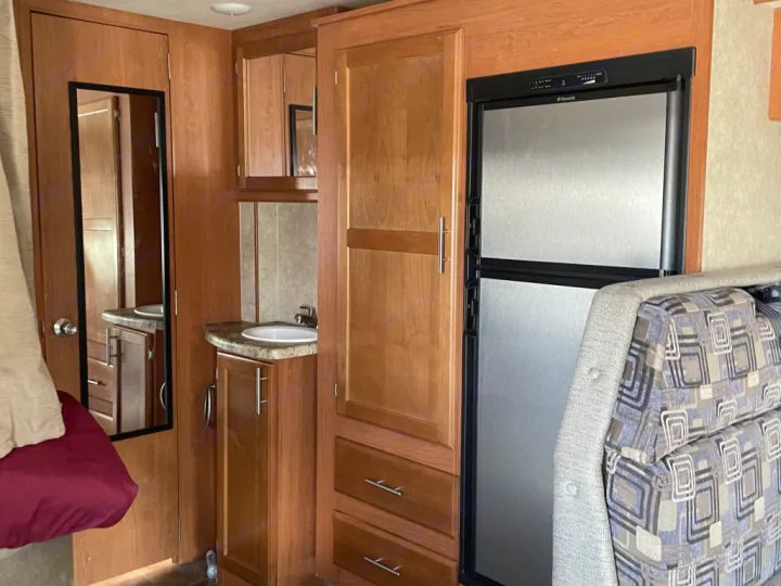 RV rental interior showing a compact bathroom with sink & mirror, a refrigerator, and a patterned dinette.. Adventurer Adventurer Motorhome 2017
