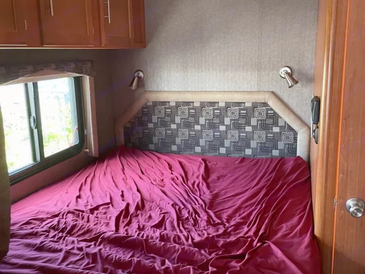 Experience an RV rental: bedroom with red-covered bed, patterned headboard, window, and overhead cabinets.. Adventurer Adventurer Motorhome 2017