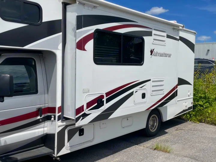 White Adventurer RV rental, side view, showing a slide-out, windows, and decorative red/black/grey stripes. Outdoor parking.. Adventurer Adventurer Motorhome 2017