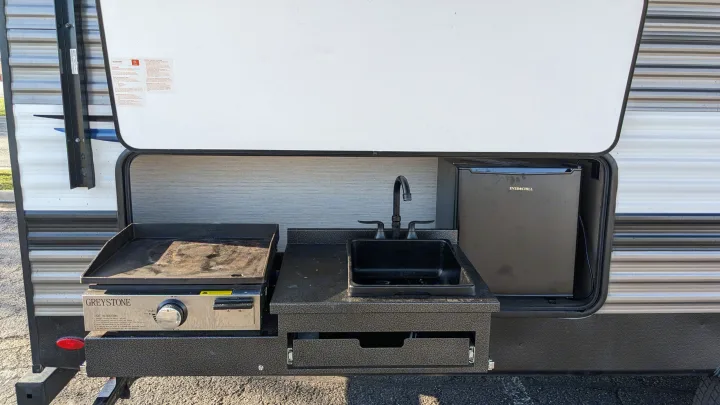 View of an RV rental's outdoor kitchen featuring a griddle, sink, and mini-fridge, ideal for convenient camping.. Forest River Palomino Puma XLE 2022