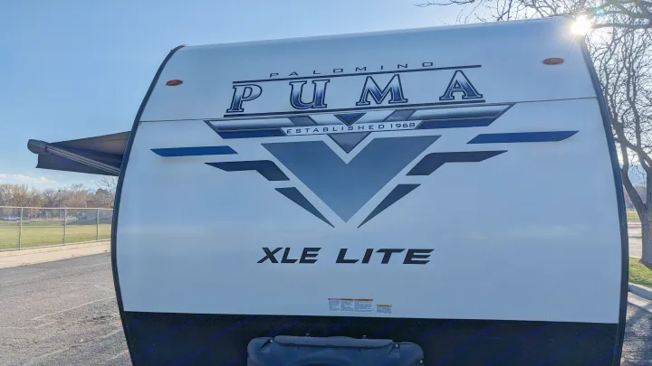 A white Palomino Puma XLE Lite RV, perfect for an rv rental, features an awning extended on a sunny day.. Forest River Palomino Puma XLE 2022