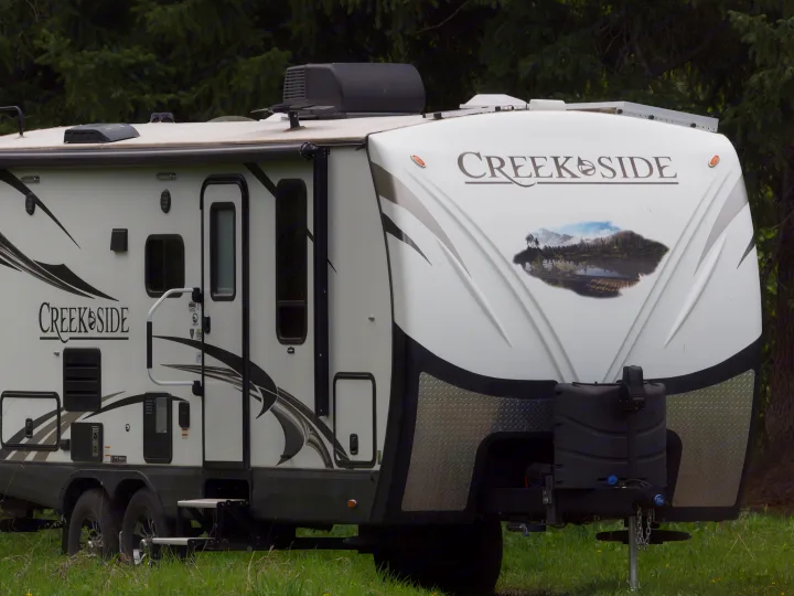 A white Creekside RV rental, with graphic designs and front mural, parked on green grass; ready for camping adventures.. Outdoors RV Creekside 2017