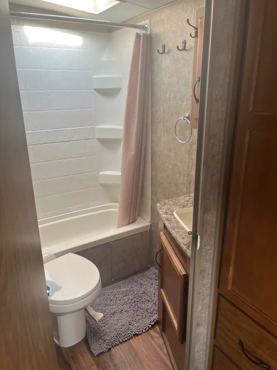 RV rental bathroom interior, showing a white tub/shower, toilet, and vanity with sink. Wooden floors & light walls.. Outdoors RV Creekside 2017