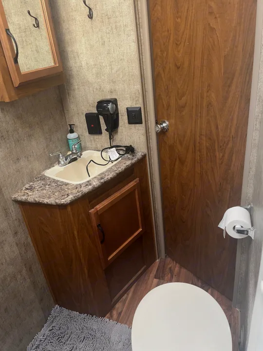 Compact RV rental bathroom: sink, vanity with mirrored cabinet, toilet, and hairdryer.. Outdoors RV Creekside 2017