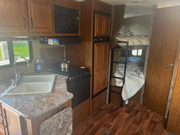 This RV rental's interior boasts a well-equipped kitchen with a sink, stove, and microwave, alongside cozy bunk beds.. Outdoors RV Creekside 2017