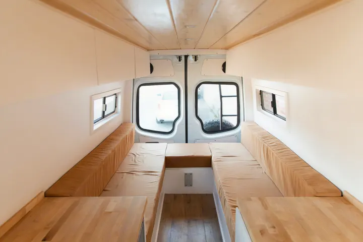 Step inside this bright RV rental! Modern camper van interior with light wood & white finishes, featuring convertible bench seating.. Mercedes-Benz Sprinter 2014
