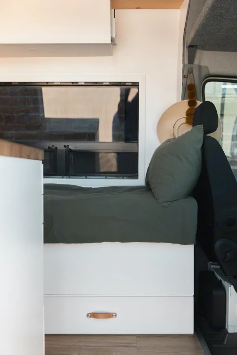 Modern RV rental interior: green bed, storage drawer with leather pull, and scenic window reflections.. Mercedes-Benz Sprinter 2014