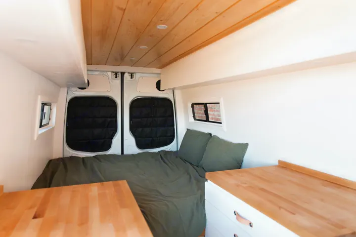 Bright RV rental interior: a bed with olive green bedding, wooden ceiling, and white built-ins create a cozy space.. Mercedes-Benz Sprinter 2014