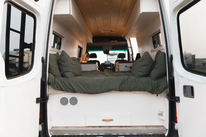 Inside a modern rv rental: a cozy bed with olive green bedding, wood ceiling, and custom storage seen from the rear.. Mercedes-Benz Sprinter 2014