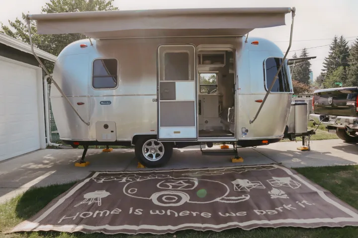 Sleek Airstream travel trailer RV rental with awning extended, door open, and "Home is where we park it" mat. Ready for camping trips!. Airstream Bambi 2023