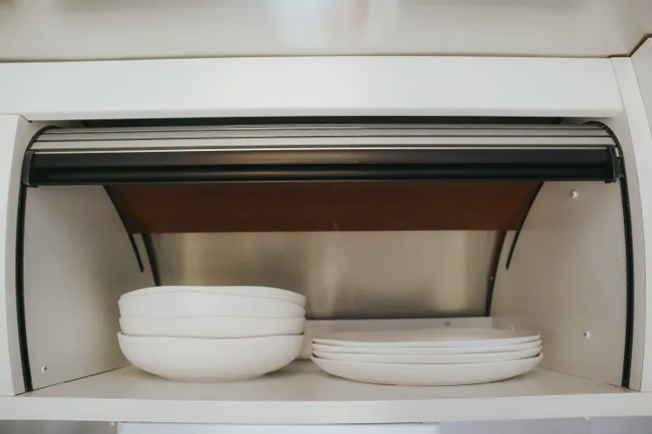 Organized white plates and bowls inside a compact kitchen cabinet with a roll-up door, perfect for your RV rental adventure.. Airstream Bambi 2023