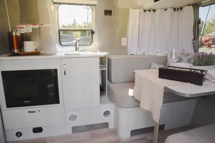 Modern RV rental interior: kitchen with microwave & sink, plus a cozy dining booth with a table.. Airstream Bambi 2023