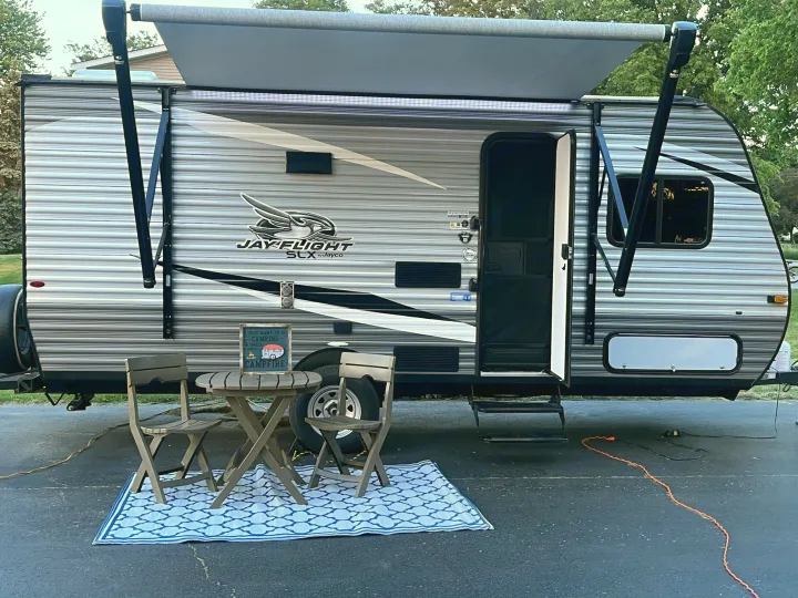 A Jayco travel trailer, ideal for an rv rental, is parked with its awning extended, a cozy patio rug, table & chairs setup.. Jayco Jay Flight 2021