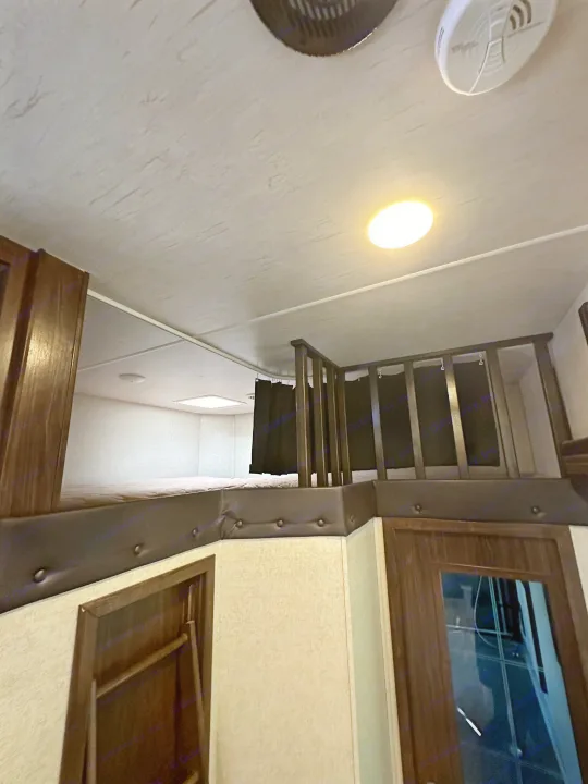 Comfortable RV rental loft bunk bed with dark wood railings and privacy curtains, perfect for extra sleeping space.. Heartland Torque 2018