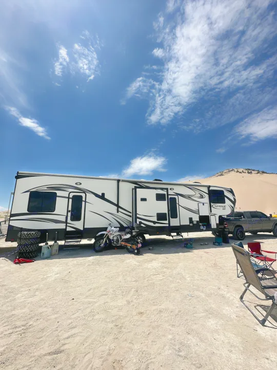 Enjoy off-road fun! This RV rental toy hauler is parked with a pickup truck and dirt bike at a desert campsite under blue skies.. Heartland Torque 2018
