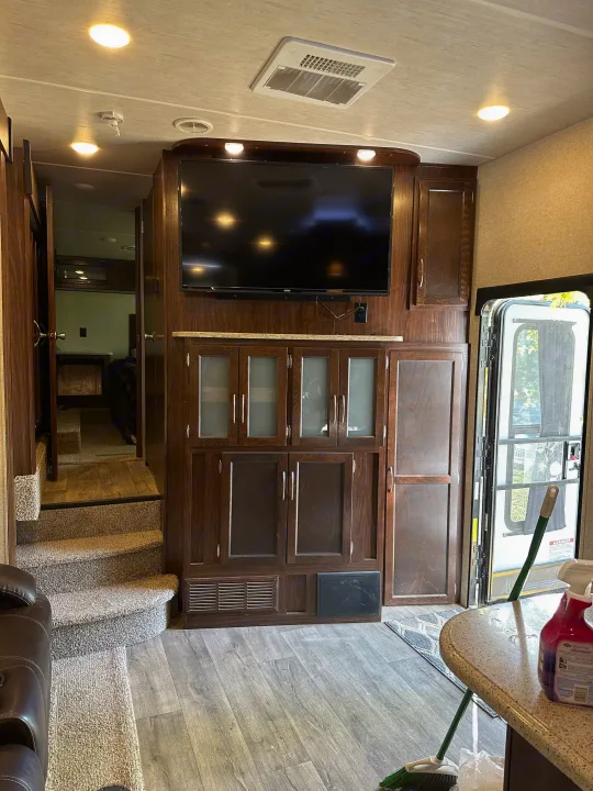Inside a modern RV rental: dark wood cabinetry, large TV, steps to sleeping area, and an exterior door.. Heartland Torque 2018