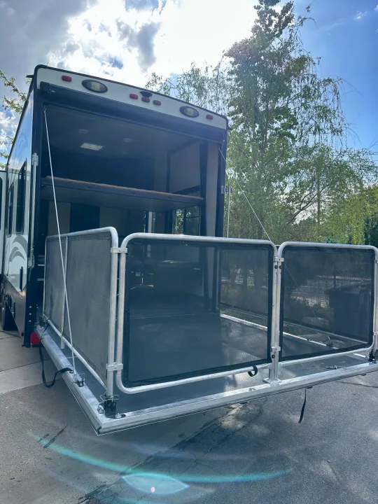 This RV rental toy hauler shows its rear ramp lowered, forming a deck patio with mesh railings, perfect for outdoor relaxation.. Heartland Torque 2018