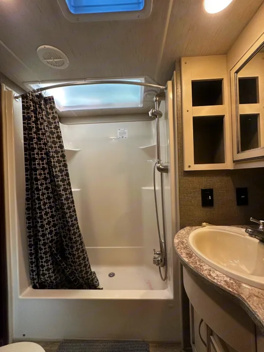 Inside an RV rental: a compact bathroom featuring a shower with a patterned curtain, and a sink vanity.. Heartland Torque 2018