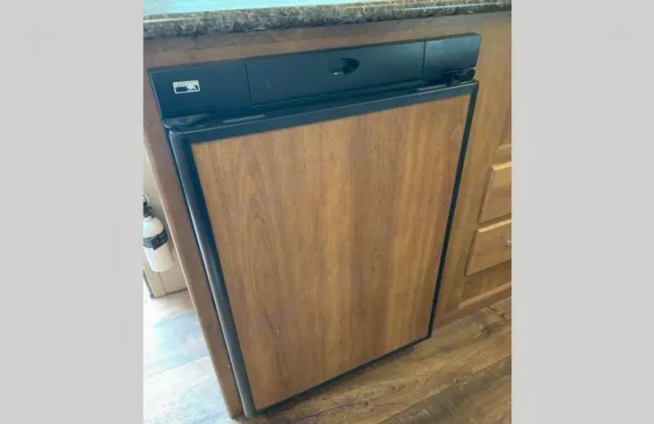 Compact RV refrigerator with wood panel door in an RV rental interior, showing practical space.. Keystone RV Summerland Mini 2017