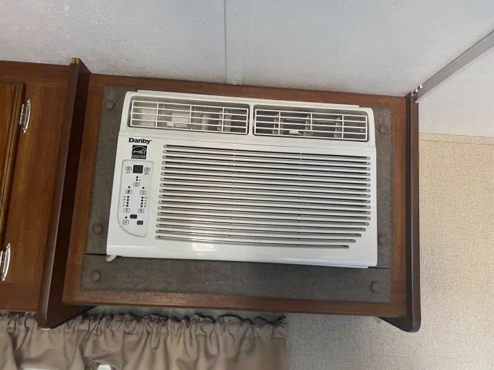 Interior view of an RV rental showing a white Danby air conditioner mounted in wood cabinetry.. Keystone RV Summerland Mini 2017