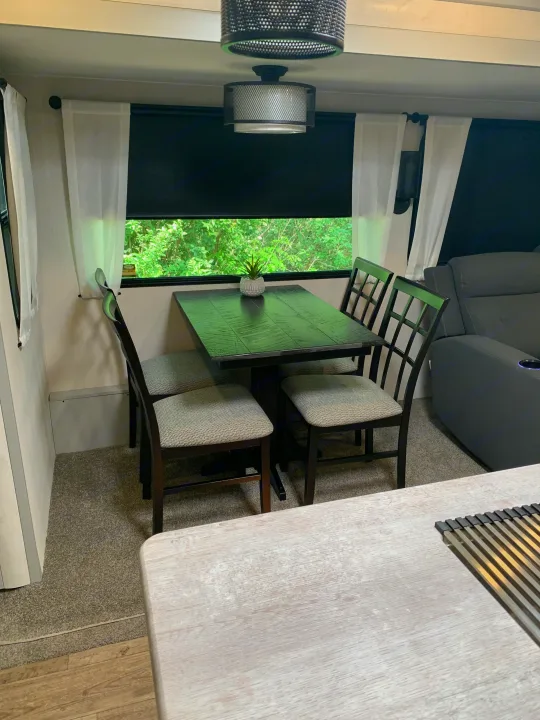 Cozy RV rental interior showing a dinette with dark table, upholstered chairs, and a window view.. Forest River Vibe 2023